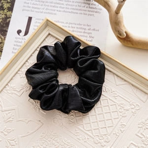 Detail of a black ruffled hair scrunchie with glossy texture on a decorative background
