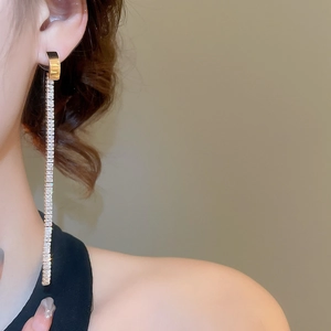 Detail of long gold linear fringe earrings featuring square-cut sparkling zircon stones