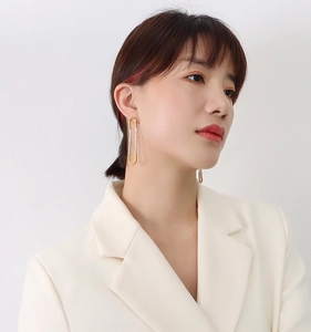 Close-up of elegant gold U-shaped earrings with zircons worn by a model in a white suit