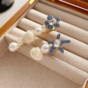 Détail de barrettes étoile de mer et fleur avec cristaux bleus et perles sur velours beige