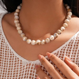 Detail of beaded necklace with white and brown marble texture on model neck