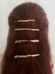 Detail of four gold wavy metal hair clips styled on long hair in a vertical row