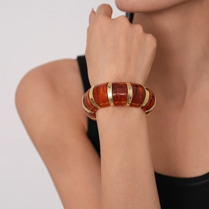 Detail of amber acrylic and gold metal wide link bracelet on model wrist