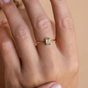 Detail of a thin gold ring featuring a rectangle light green gemstone in 4-prong setting