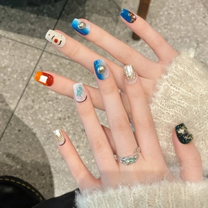 Press-on nail set featuring orange and blue artistic patterns with emerald ring on hand