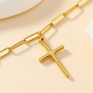 Close-up of golden paperclip chain necklace featuring a minimalist cross pendant detail