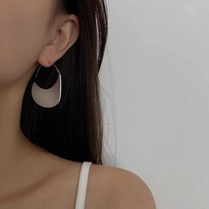 Dettaglio di orecchini a cerchio a mezzaluna in argento opaco indossati con stile minimal