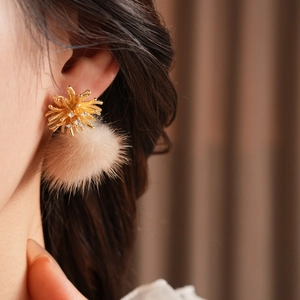 Close-up of golden fireworks zircon earrings with soft beige fur balls worn by a model