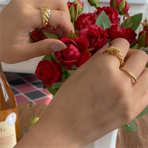 Set of gold croissant and twisted rope rings worn by hand amidst red roses