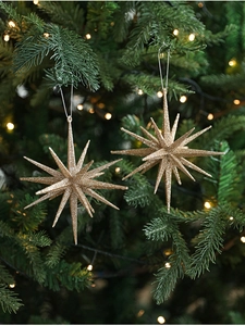 Golden glitter starburst Christmas tree ornaments hanging on green pine branches