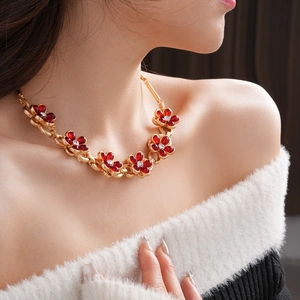 Detail of a vintage style gold necklace featuring a red crystal floral pendant on model