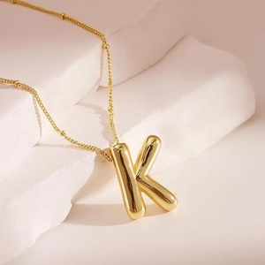 Macro detail of golden bubble letter K pendant on textured stone background