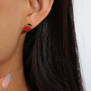 Close-up of red rhinestone strawberry stud earring with gold base on a model's ear