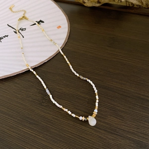 Detail of beaded necklace featuring white seed beads and an opal pendant on wood