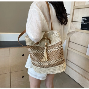 Detail of a striped beige straw tote bag with brown tassel and shoulder strap