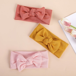 Flat lay of three ribbed knit baby headbands with large bows in pink and mustard yellow
