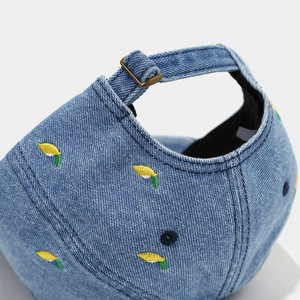 Close-up of denim baseball cap with lemon embroidery and adjustable metal buckle strap