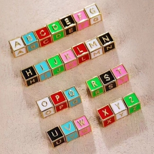 Detailed view of colorful enamel A-Z alphabet cube beads with golden metal frames for DIY