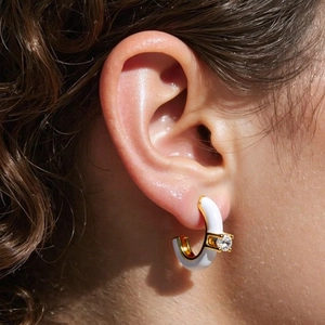 Close-up of C-shaped white enamel earring with gold base and sparkling zircon on ear