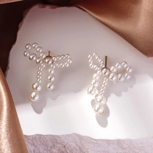 Detailed macro shot of bow pearl earrings with long tassels on silk fabric