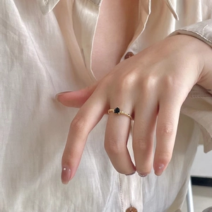 Detail of a gold rope-textured ring with a black heart stone worn on a model's finger