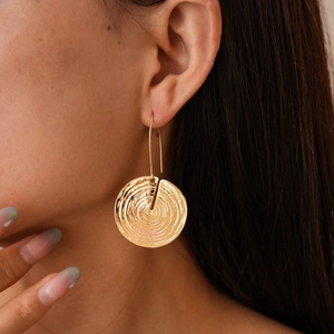 Macro shot of gold circular earrings with spiral texture on a model's ear