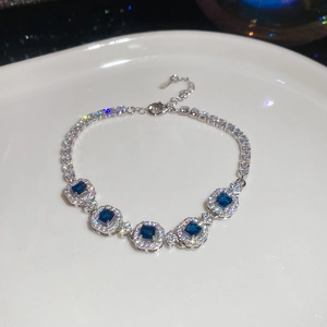 Macro detail of silver tennis bracelet with square blue gemstones and halo zircon settings