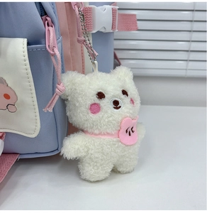 Close-up of a white plush bear pendant with pink heart bib on a colorful backpack