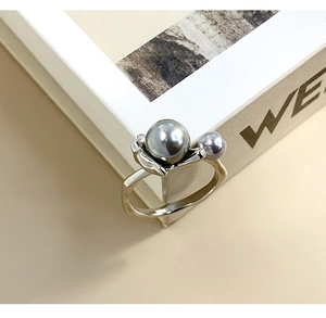 Detail shot of silver flower ring with grey and purple pearls on a beige book