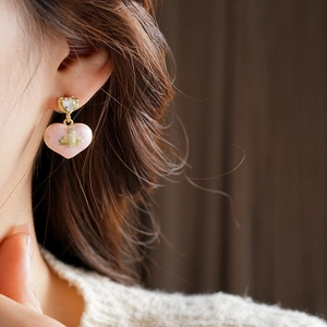 Close-up of model wearing pink heart-shaped drop earrings with gold finish and small gems