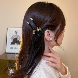 Close-up of black velvet hair clip with a gold-trimmed camellia flower and pearl accent