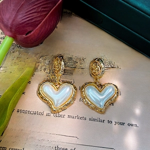 Detail of golden heart earrings with white pearlescent inlay on a vintage book page