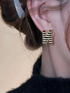 Close-up of a 18K gold plated 'H' letter stud earring with black enamel and zircons
