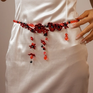 Detail of red and black floral beaded waist chain with tassels on a white dress