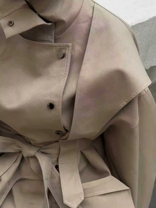 Detail view of beige trench coat featuring stand-up collar, metal buttons and waist belt