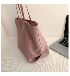 Detail of pink nylon tote bag with metal logo on a desk next to a laptop