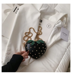 Detail of strawberry-shaped crossbody bag with gold studs and green leaf top decoration