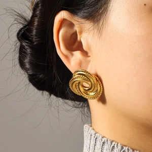 Détail macro de boucles d'oreilles dorées à texture spirale portées par un mannequin