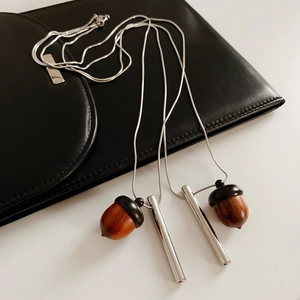 Detail of silver snake chain necklace with brown wooden acorn and metallic cylinder pendant