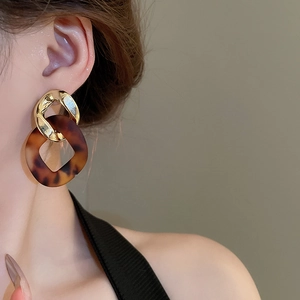 Close-up of model wearing geometric gold chain earrings with brown tortoiseshell resin