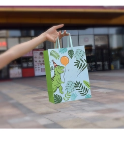 Detail of cute dinosaur gift bag with blue ribbon handle held against a soft bokeh background
