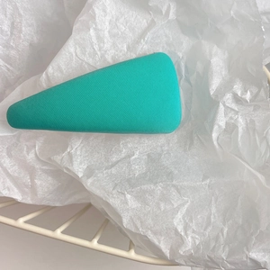 Close-up of green triangular sponge hair clip with woven texture on white tissue paper