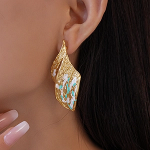 Detail of gold wrinkled leaf earring with white and turquoise enamel on a model
