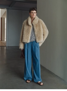 Detail of a beige faux fox fur cashmere vest paired with blue wide-leg denim jeans