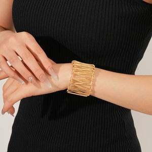 Détail d'un large bracelet manchette doré à fils enroulés porté par un mannequin en noir