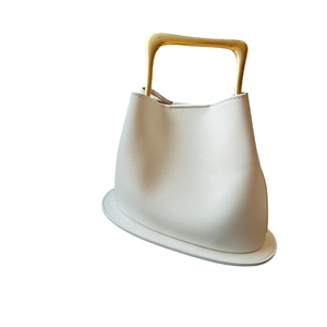 White leather bucket bag with a golden metal handle and trapezoid shape on white background