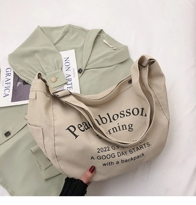Détail du sac cabas en toile crème avec lettrage noir et bandoulière à boucle réglable