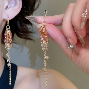 Macro detail of amber crystal drop earrings with long gold tassel chains for women