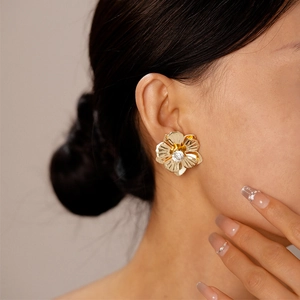 Vue détaillée de boucles d'oreilles fleur dorée avec cristal porté par un modèle