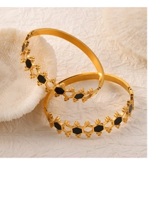 Detail view of gold honeycomb bangles with black enamel inlay on white coral background